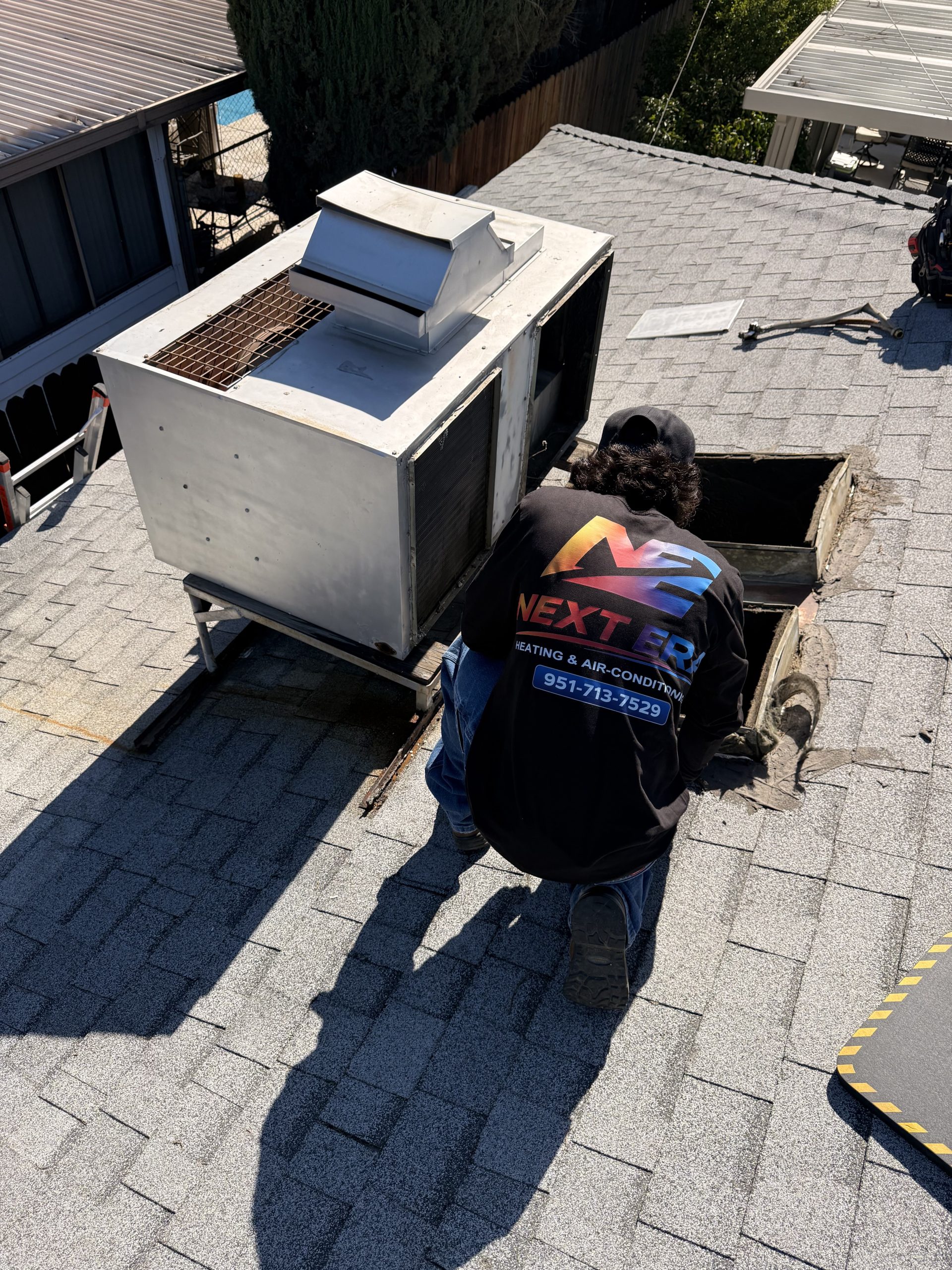 Next Era technician working on a rooftop package unit and duct opening
